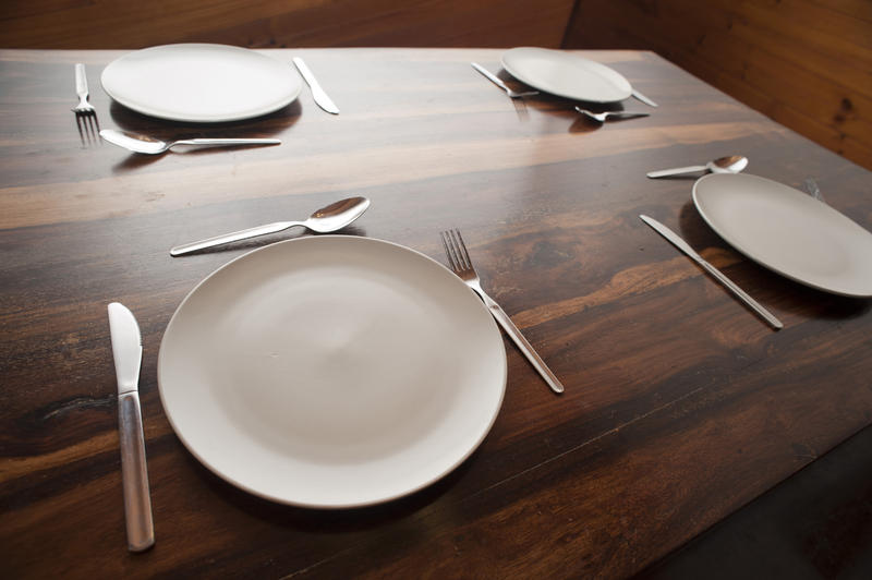 Wooden dining table with four place settings with empty white plates and cutlery laid directly on the wooden surface