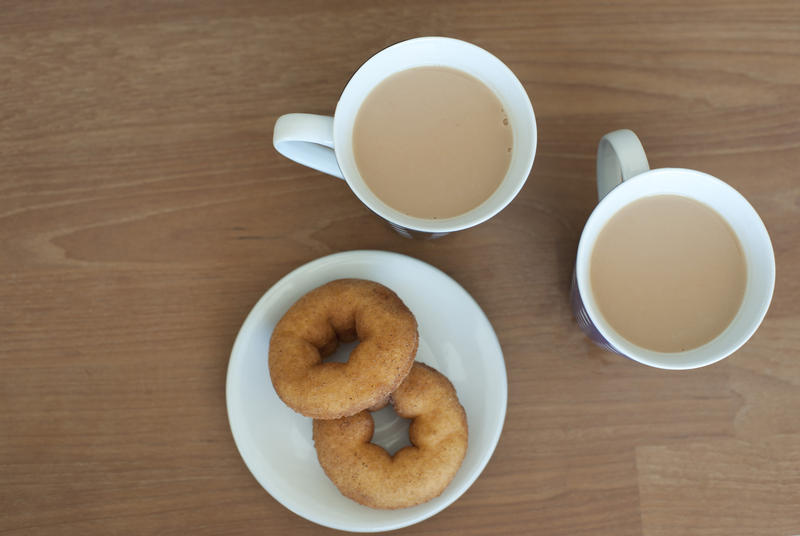 Aerial View of Cups of Creamy Coffee and Plate of Doughnuts on Side Served on Brown Wooden Table