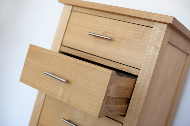 Small wooden chest of drawers or cabinet with metal handles and one open drawer, tilted angle view