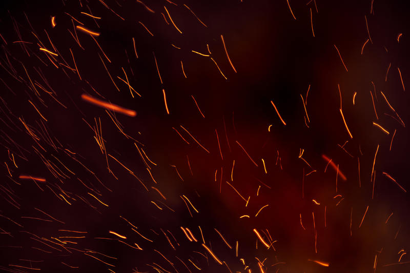 Background of fiery trails from glowing embers shooting through the darkness from a burning bonfire