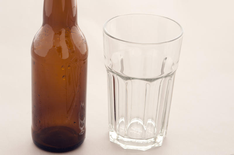 Empty glass with an unlabeled brown bottle of beer alongside on a white background