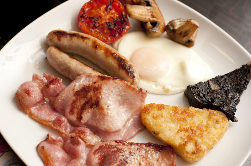 Hearty traditional English breakfast with a fired egg, sausages, bacon, mushrooms, tomato and hash browns