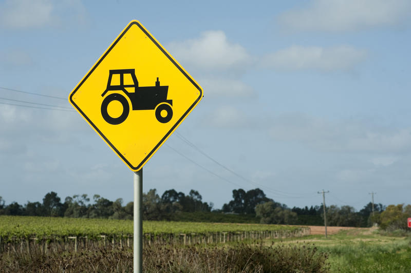 Close up Black and Yellow Traffic Farm Sign with Tractor Symbol In Front of a rural landscape
