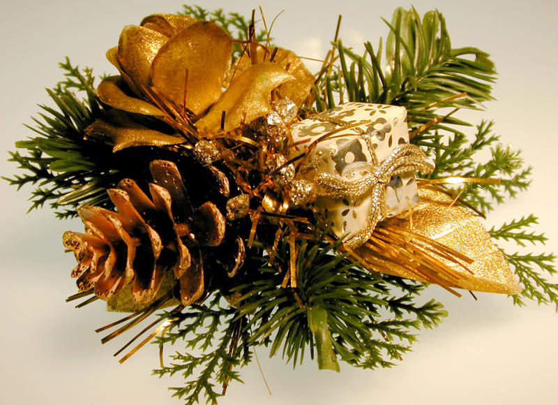 Gold festive Christmas bundle decoration with a rose, pine cone gift and bow nestled in green foliage, close up view