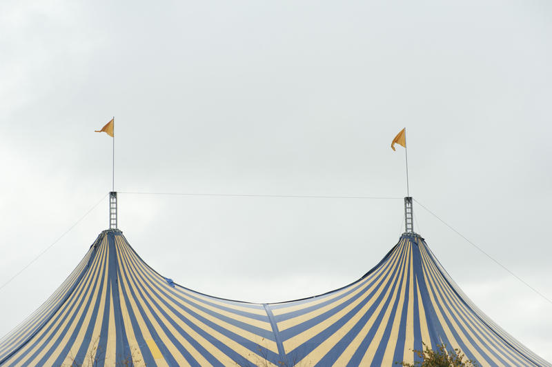 Striped top of a Big Top Circus tent flying two flags from the tent poles for performing acts