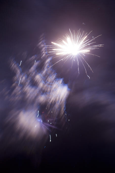Fireworks display with wafting smoke as a bright white rockets bursts in a shower of fiery sparks in a night sky