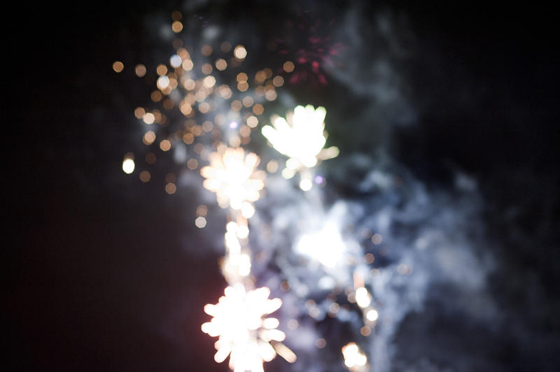 Festive bokeh of defocused bursting fireworks in a night sky during a holiday celebration with copyspace to the left side