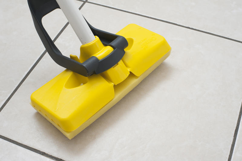Close up view of washing and mopping the tiled white floor with a colorful yellow plastic squeegee in a hygiene and household chores concept