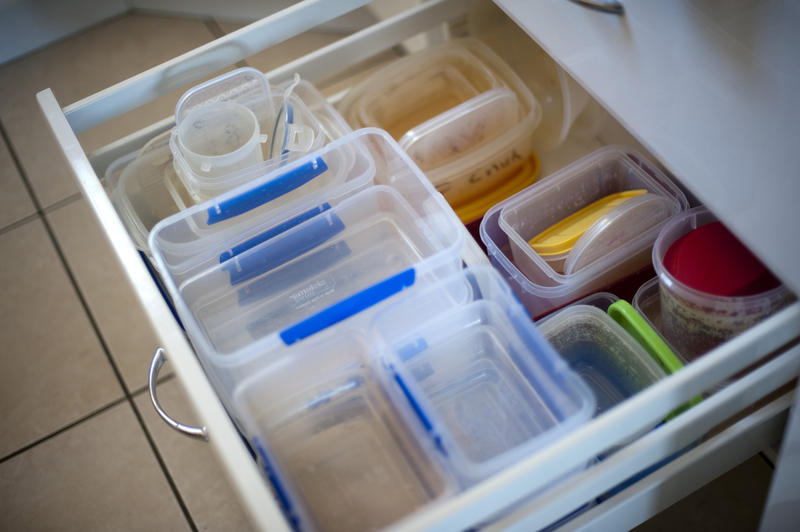 Plastic food storage containers neatly stacked in an open drawer in a kitchen cabinet