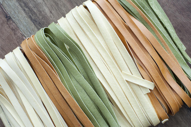 Multicolored variations of fettuccine Italian pasta in green , white and brown dried ribbons packaged in alternating colors for use as an ingredient in Italian cooking, high angle view of the texture