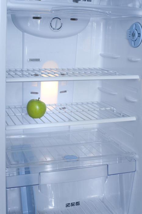 View of the interior of small domestic a fridge with wire shelves and plastic drawers with a single green apple in the otherwise empty interior