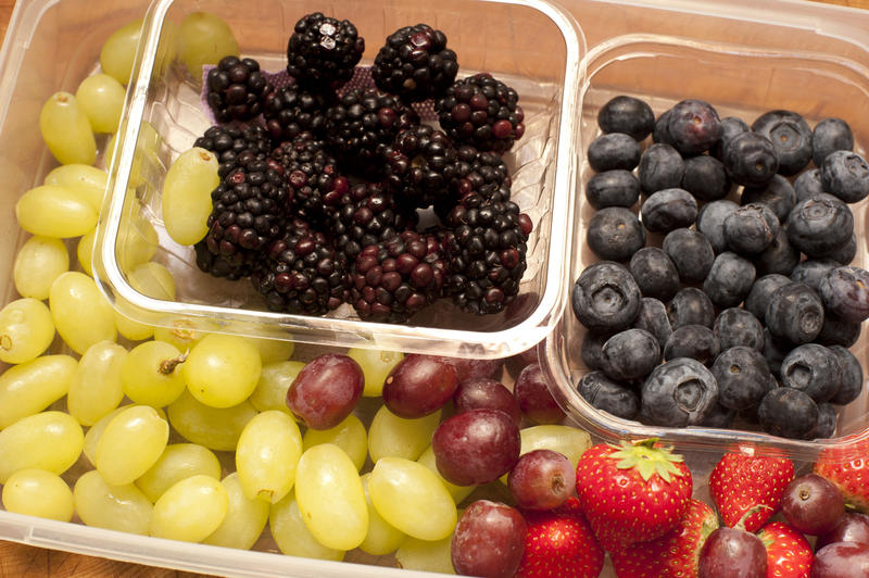 Punnets of fresh fruit with green and purple grapes, blueberries blackberries and strawberries , closeup high angle view