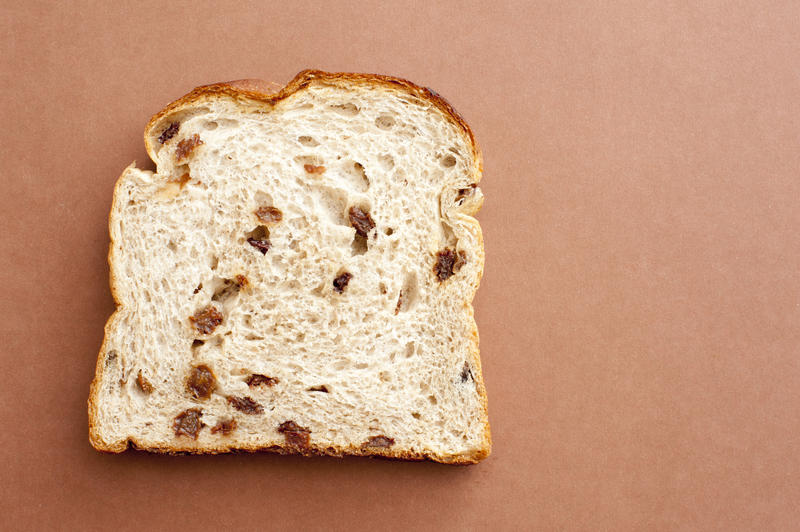 Slice of white fruit bread with raisins lying on a brown background with copyspace, overhead view