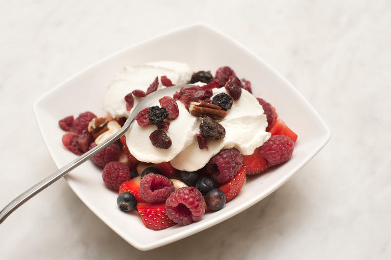 Bowl of fresh fruit with assorted berries and raisins topped with healthy plain yoghurt for a scrumptious dessert or breakfast