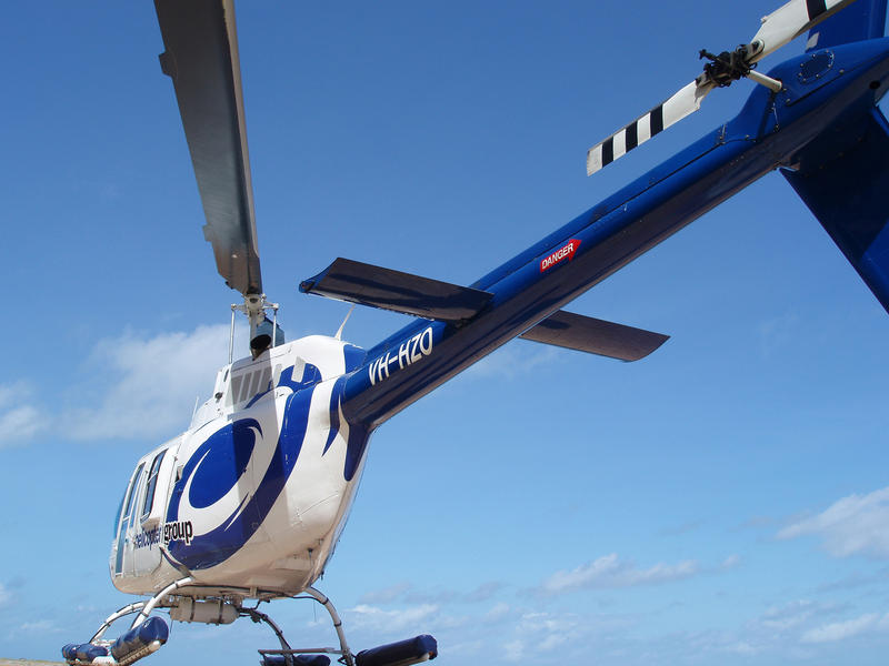 Low angle view of a blue and white helicopter parked on a helipad against a blue sky - no ground visible