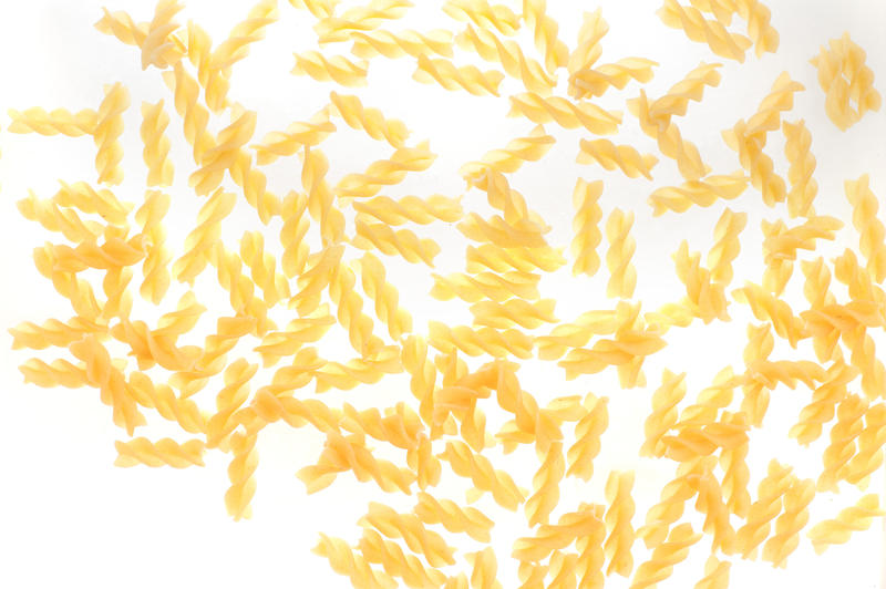 Scattered dried fusilli pasta with its distinctive spiral shape for use in traditional Italian cuisine on a white background