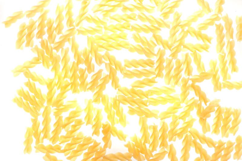 Backround pattern of Italian fusilli pasta with its twisted spiral shape scattered randomly on a white background, viewed from above