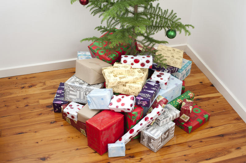 Pile of Christmas gifts st the base of a tree in different shapes and sizes wrapped in colourful wrapping paper with traditional patterns