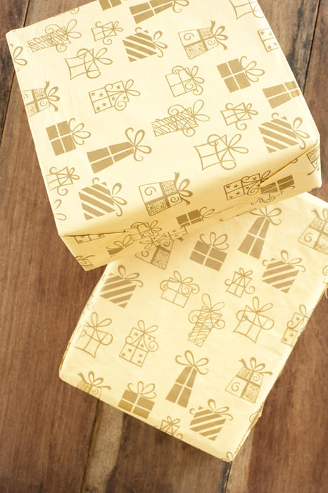 Two gift-wrapped party gifts in pretty decorative cream colored paper with a generic pattern of different gift boxes viewed from above on a wood background