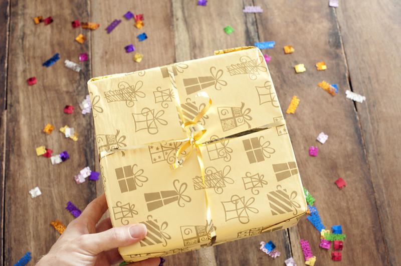 Overhead view of the hand of a man giving a birthday gift in pretty gift wrap over a wooden table background with scattered Happy Birthday sprinkles or confetti