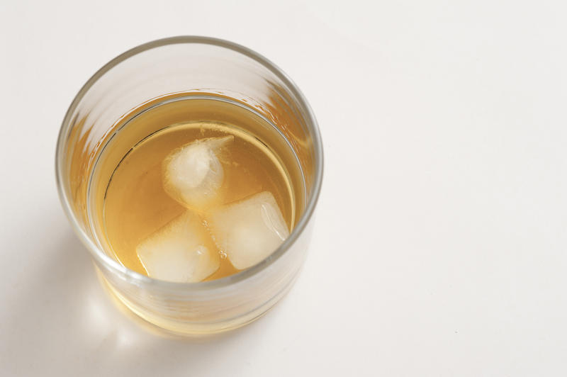 Glass of whiskey served with ice in a glass tumbler viewed from above on a white background with copyspace