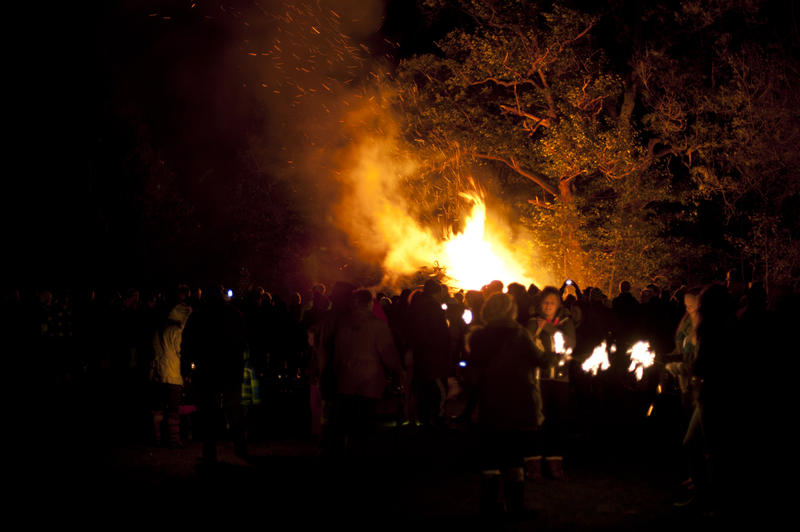 Crowd standing grouped in a field at night watching a roaring bonfire on Guy Fawkes with fiery orange flames leaping into the air - not model released