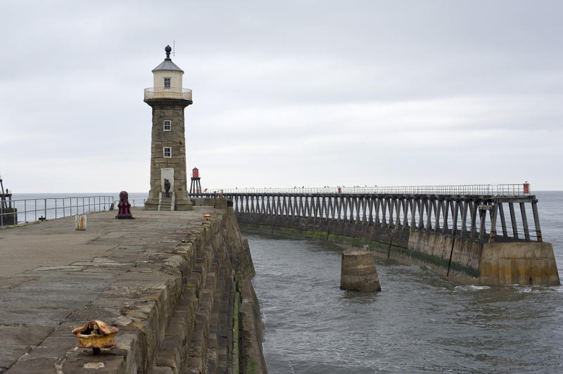 View of the old stone lighthouse at the end of the East pier at Whitby harbour with the breakwater alongside
