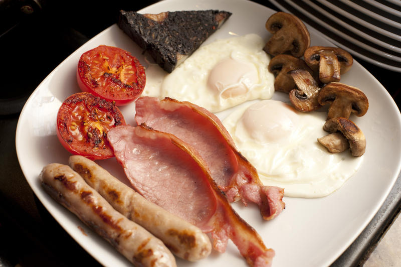 Hot traditional English breakfast with fried eggs, bacon, mushrooms, tomato, black pudding and sausages served on a plate