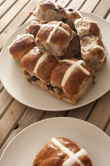 Batch of freshly baked Hot Cross Buns for celebrating Easter served on a white plate on a slatted wooden table, high angle view