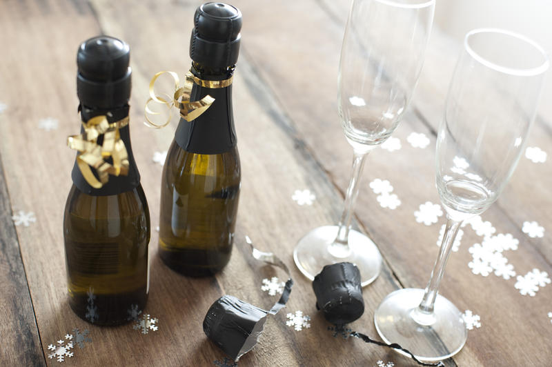 Individual Champagne Bottles and Glasses on Top of Wooden Table with Snowflakes.
