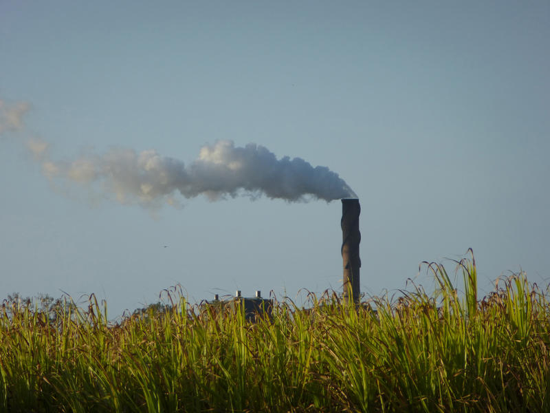 View across a rural green field of an industrial chimney belching smoke into the air polluting the atmosphere in an environmental concept