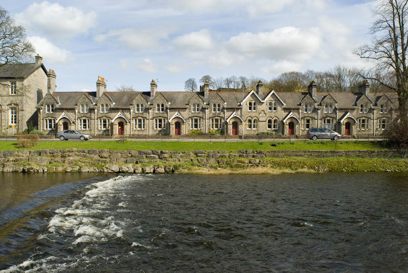Weir at Kendal on the river Kent overlooked by a riverside row of terraced stone townhouses