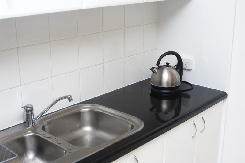 Small kitchen with double stainless steel sink unit, black countertop and white tiles as a splashback with a kettle on the counter