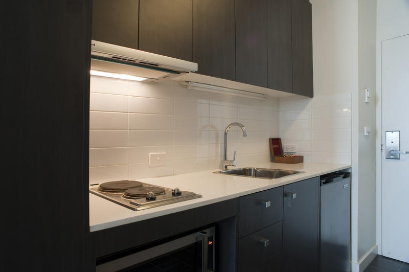 Interior of a modern compact kitchen with black cabinetry and a white tiled splashback above a white counter with hob and sink