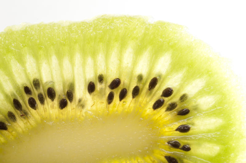 Macro detail of a slice peeled kiwifruit showing the interesting natural pattern of the juicy green flesh and pips on a white background