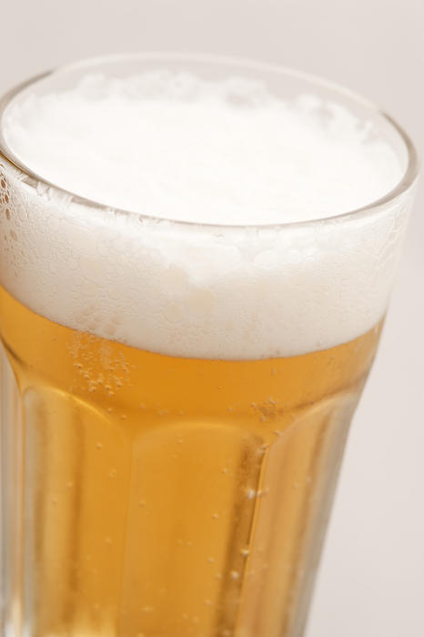 Glass of cold fresh beer with froth, close-up on grey
