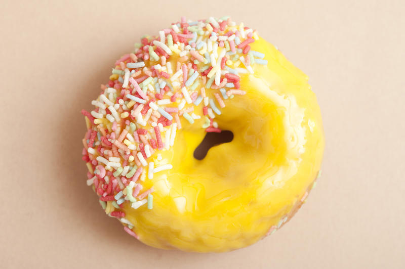 Glazed lemon ring doughnut with colorful citrus icing dipped in multicolored sprinkles on one side, overhead view on a neutral background