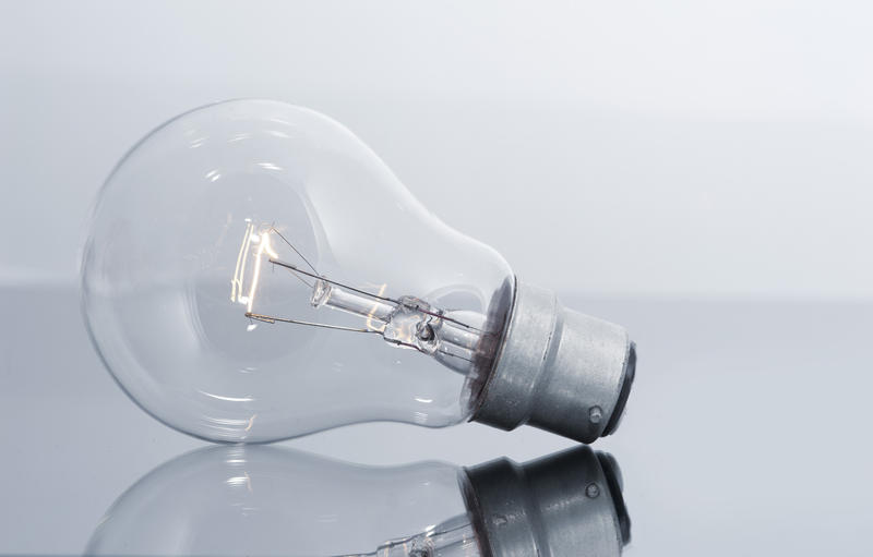Close Up Still Life of Clear light bulb with Glowing filament on Reflective Surface in Studio with Grey Background