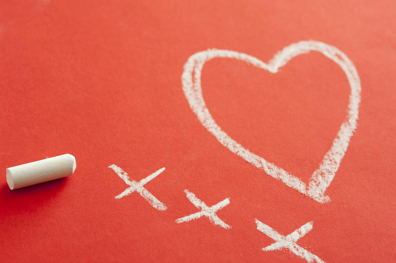Love and kisses with a symbolic drawing of a heart with three crosses drawn in chalk on a red background with copyspace for your Valentine greeting
