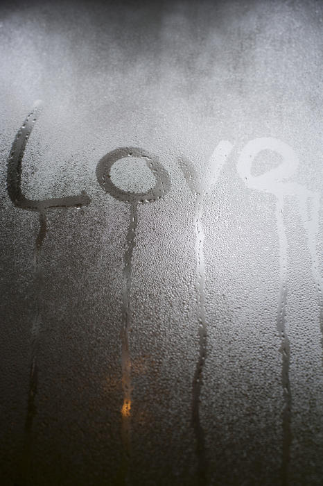 The word - Love - written in condensation on a glass windowpane with running rivulets or water and copyspace