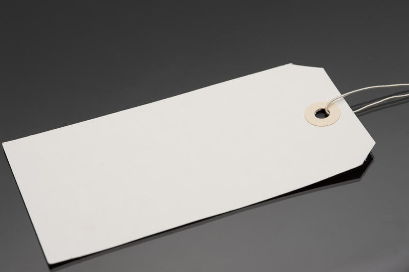 Blank cardboard gift tag or label with a string attached lying at an oblique angle on a grey background