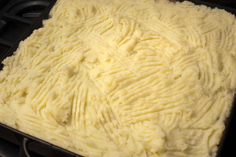 Mashed potato topping with fork lines on a cottage pie in an oven dish waiting to go into the oven under the grill