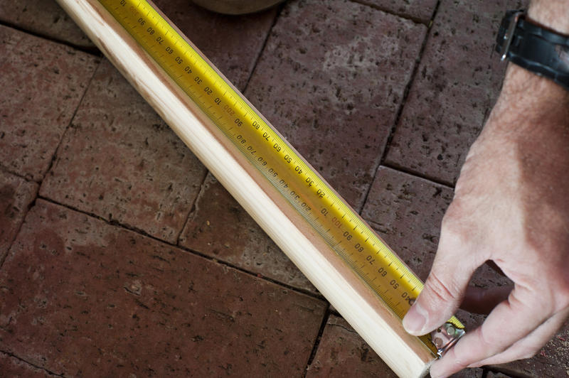 Man measuring a length of wood with a builders tape measure marked in both centimetres and inches in a DIY, woodworking and carpentry concept