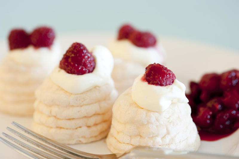 Individual mini meringue pavlovas with decorative twirled cases filled with whipped cream and topped with ripe red raspberries