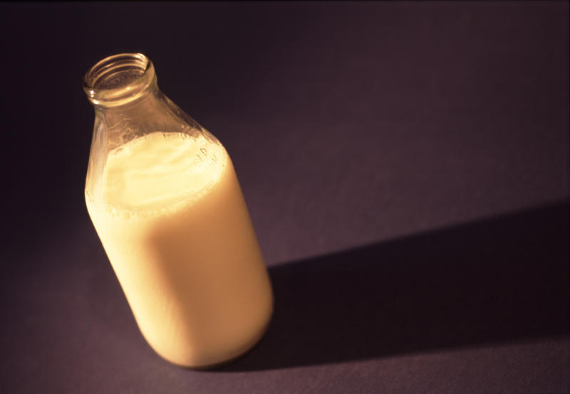 Glass bottle of cows milk with the top off on a black background with copyspace