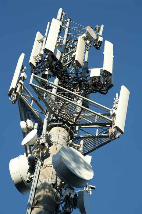 Telecommunications tower for mobile phone reception and transmission with an array of dishes and antennae against a sunny clear blue sky