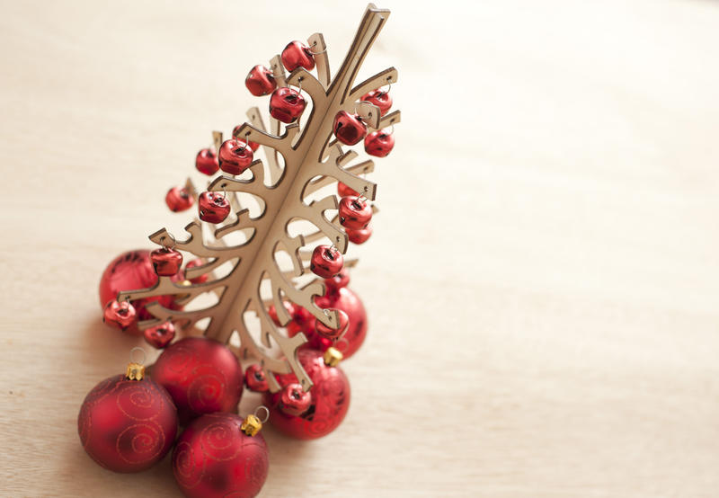 Modern Christmas tree decoration with a stylized tree hung with festive red baubles of different sizes on a light wood background with copy-space