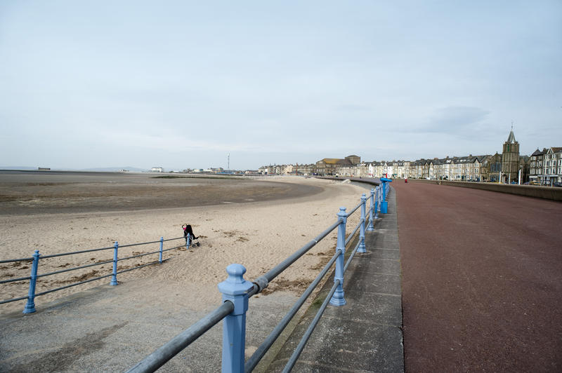 View along the Morecambe promenade and beach overlooking Morecambe Bay with a row of historical waterfront buildings visible in the distance