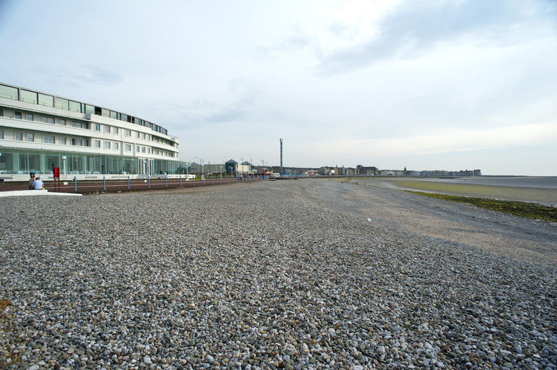 View along the deserted pebbly beach on the Morecambe shoreline with a modern commercial building on the left