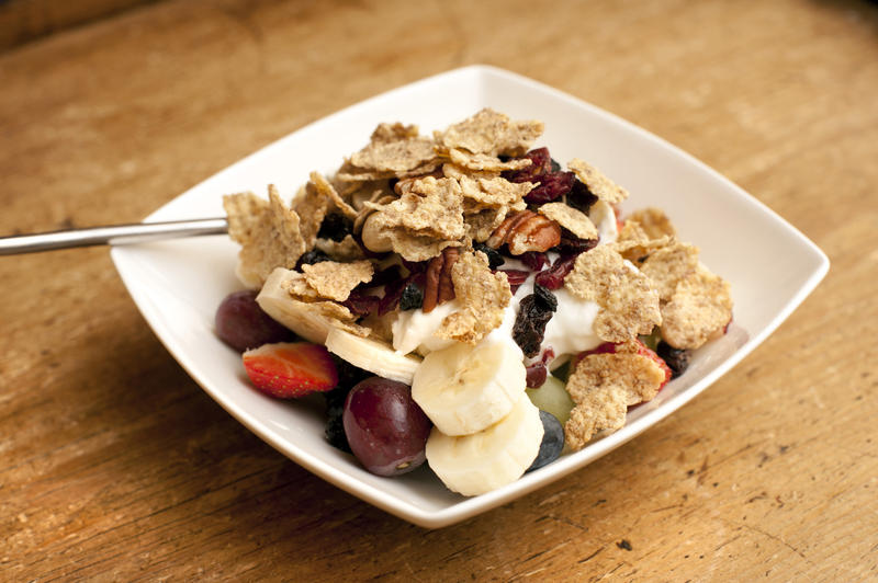 Muesli with fresh diced fruit including berries and banana served in a bowl for breakfast with a dollop of fresh plain yogurt